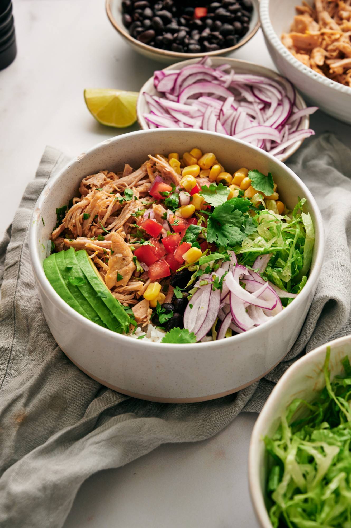 Carnitas bowl with shredded pork, corn, avocado, beans, lettuce, onions, cilantro, and avocado.