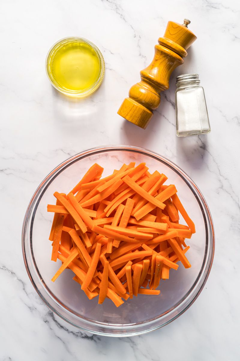 Ingredients for carrots fries including thinly sliced carrots, olive oil, salt, and pepper.