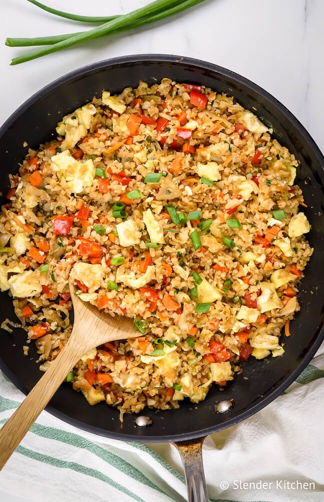 Cauliflower rice with eggs, carrots, cabbage, and green onion in a skillet.