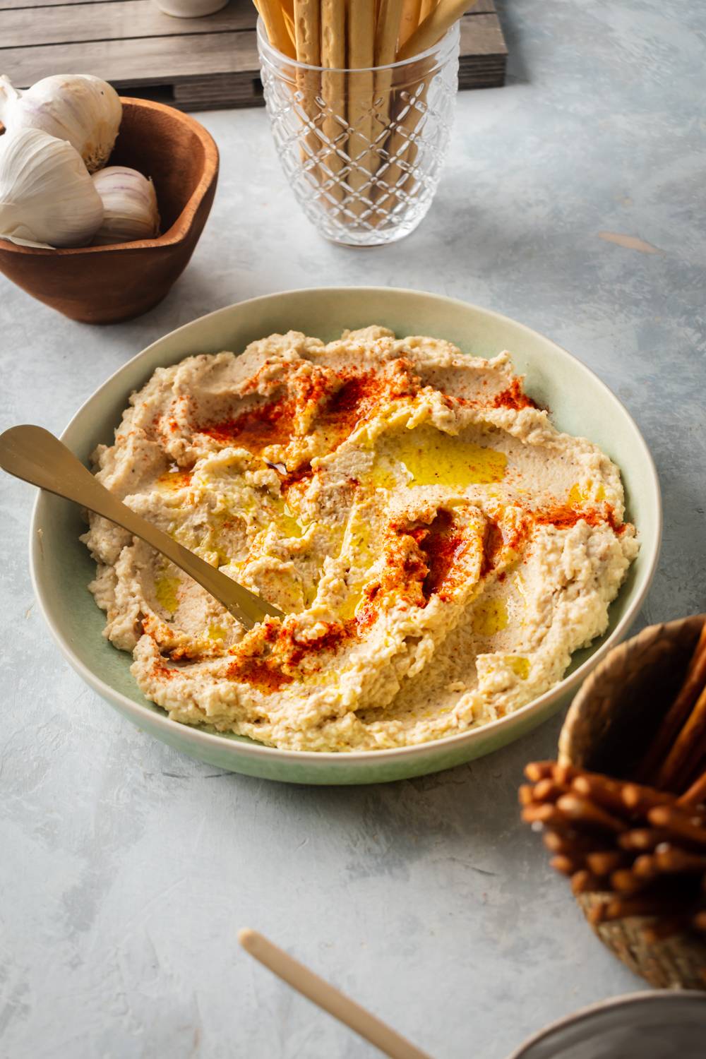 Roasted cauliflower hummus served in a bowl with olive oil and paprika with pretzels and breadsticks on the side.