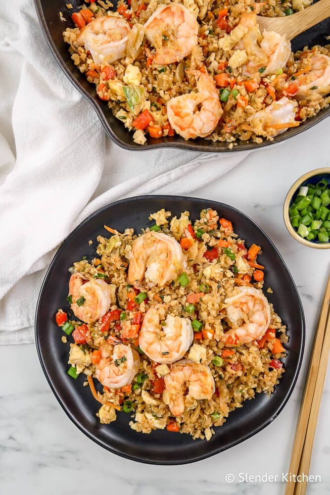 Cauliflower fried rice with shrimp, green onions, carrots, and cabbage on a plate with chopsticks.