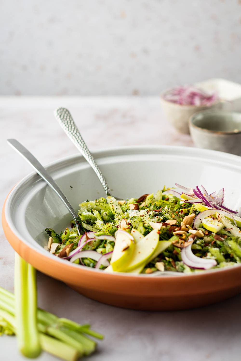 Crispy celery salad with apples, red onion, herbs, almonds, and a homemade vinaigrette in a white bowl.