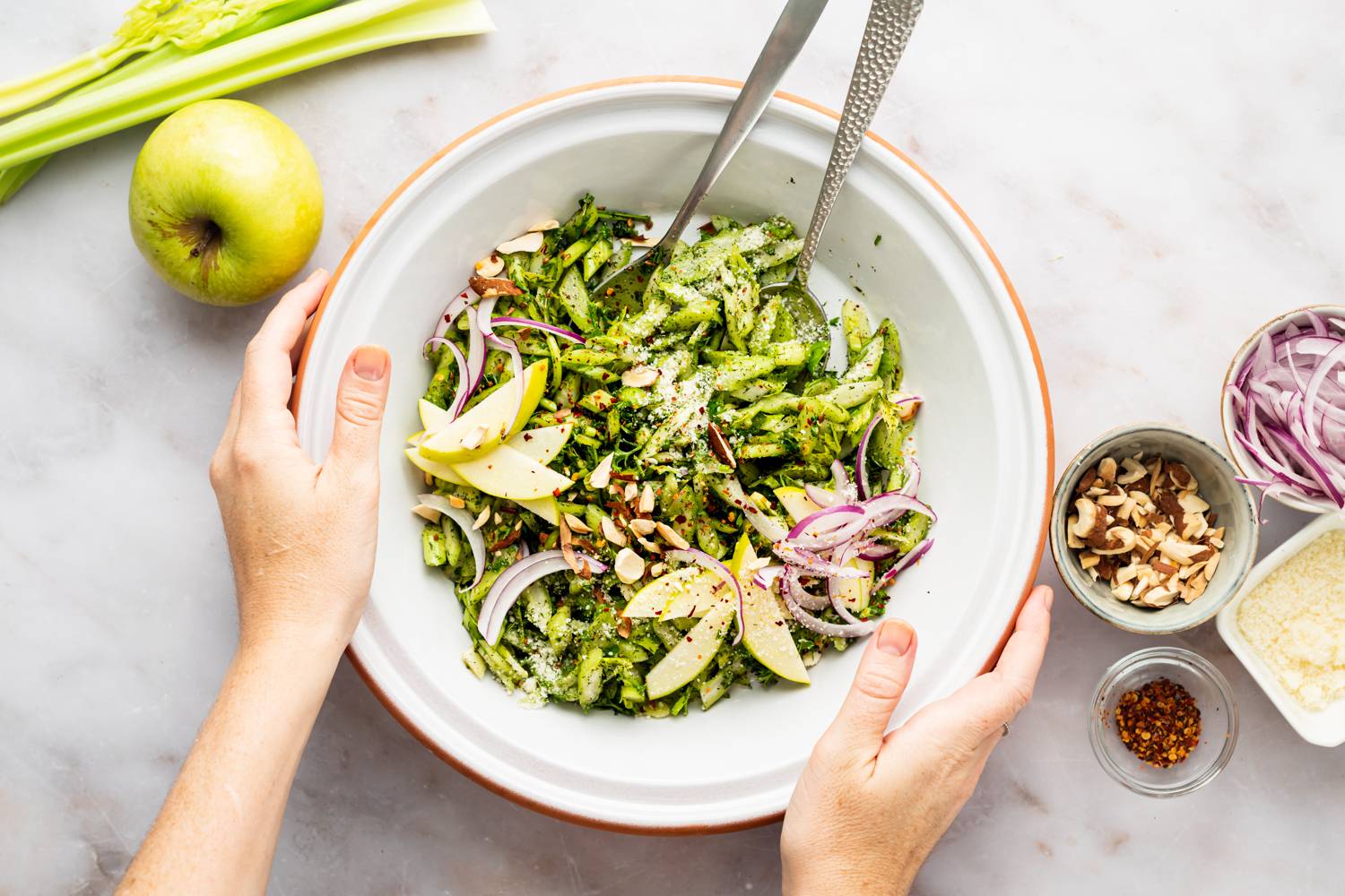 Bowl of celery salad with homemade vinaigrette, fresh herbs, apples, almonds, and red onions.