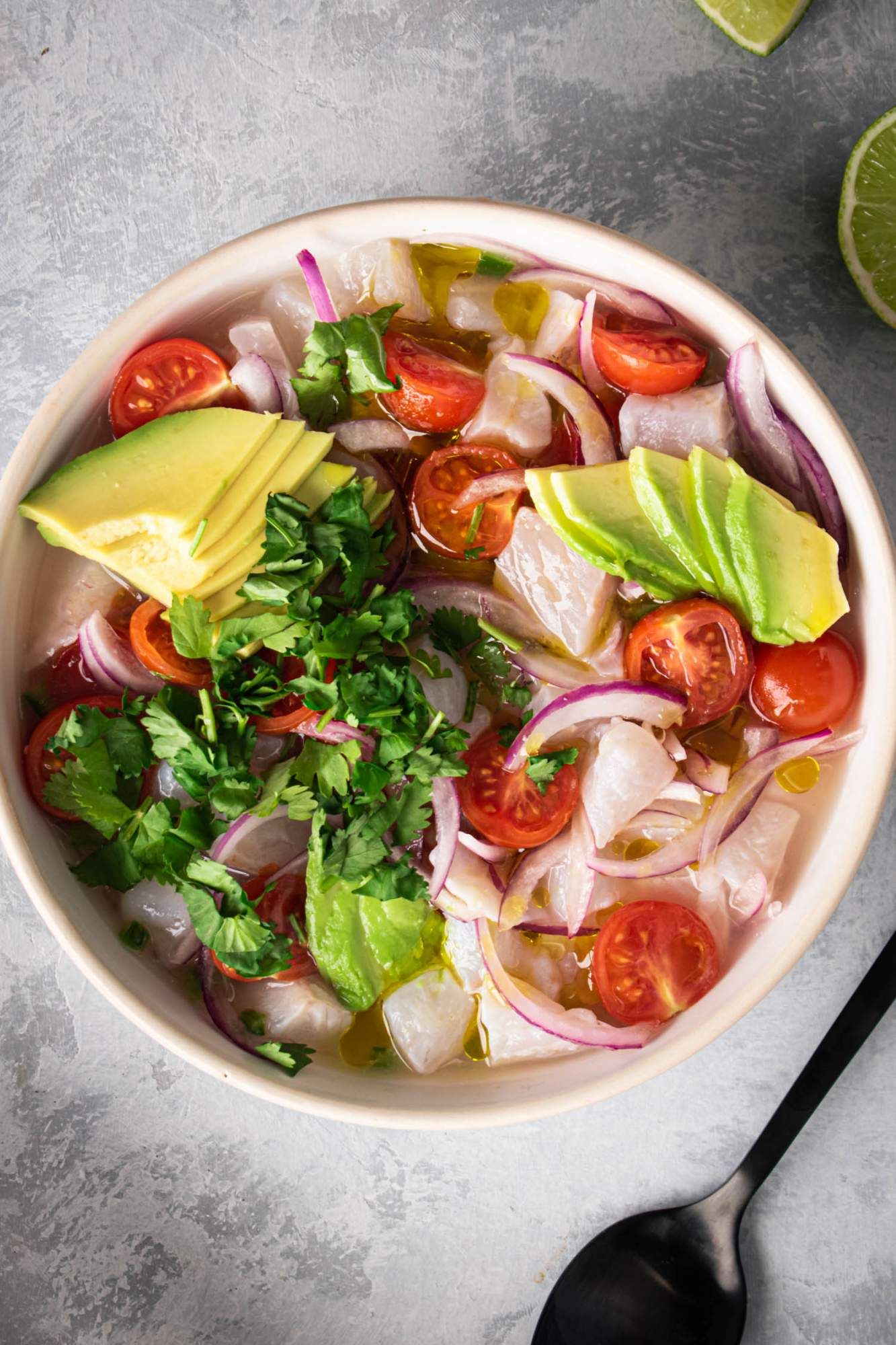 Fish ceviche with lime juice, avocados, cherry tomatoes, red onion, and cilantro in a bowl. 