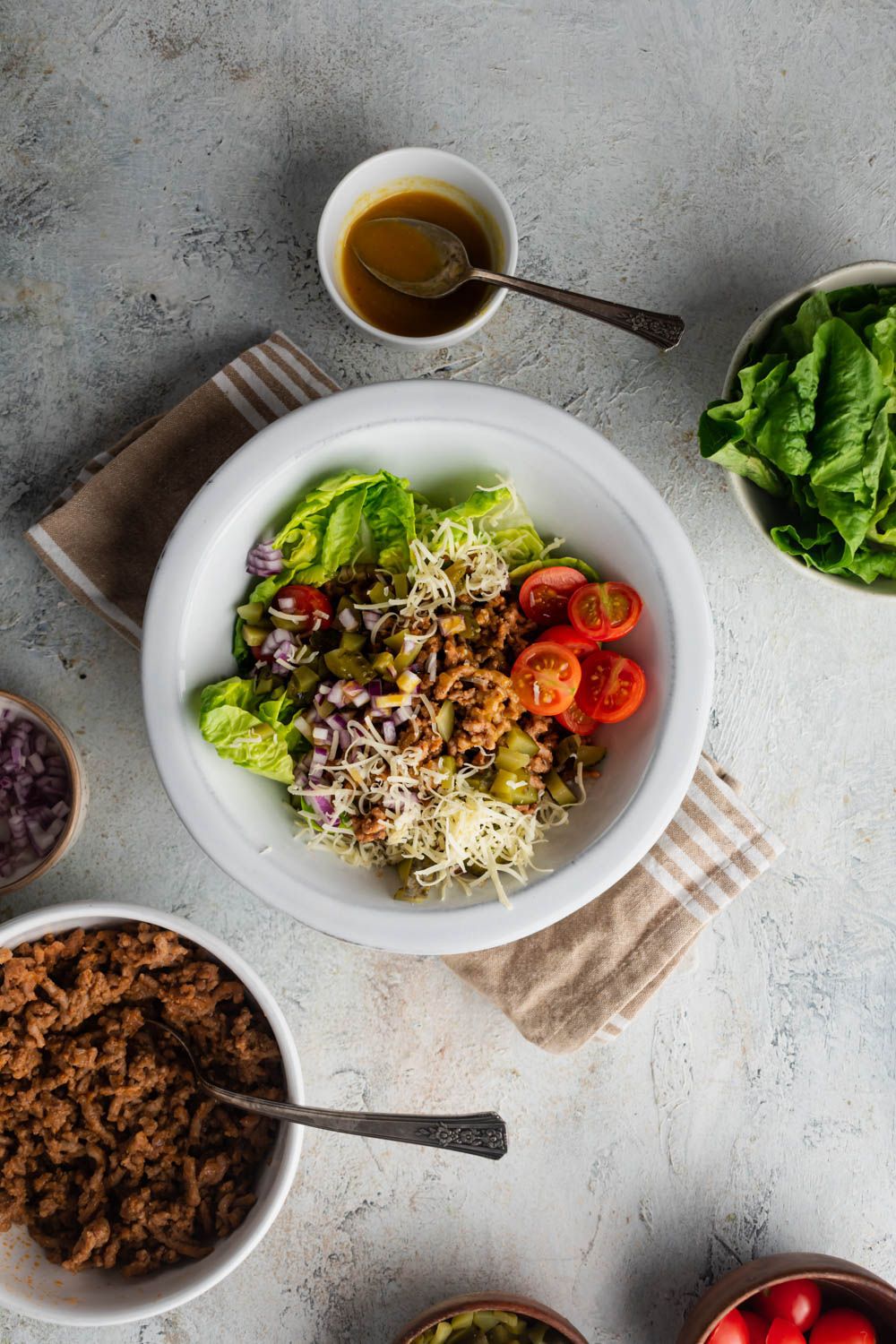 Healthy cheeseburger salad with ground beef, chopped romaine, pickles, tomatoes, and shredded cheese in a bowl with dressing on the side.