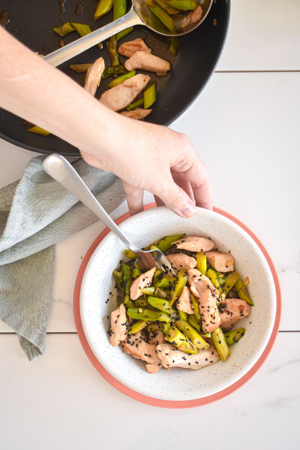 Stir fry with chicken breast and asparagus in stir fry sauce in a bowl with a hand on the side.