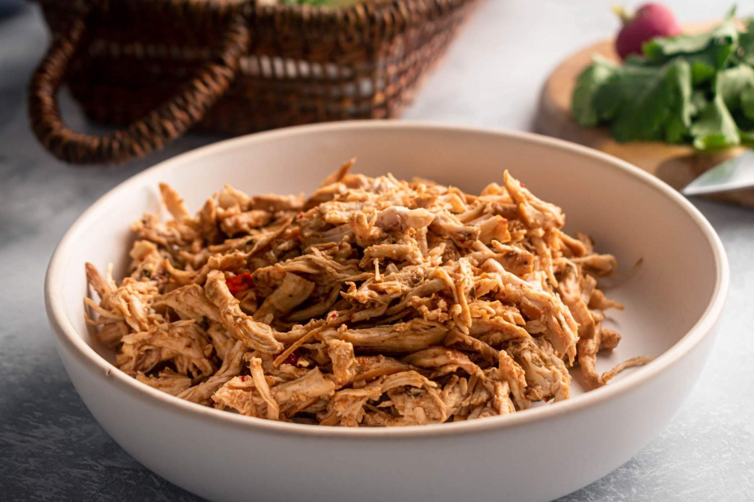 Shredded chicken barbacoa in a white bowl with barbacoa sauce and cilantro on the side.