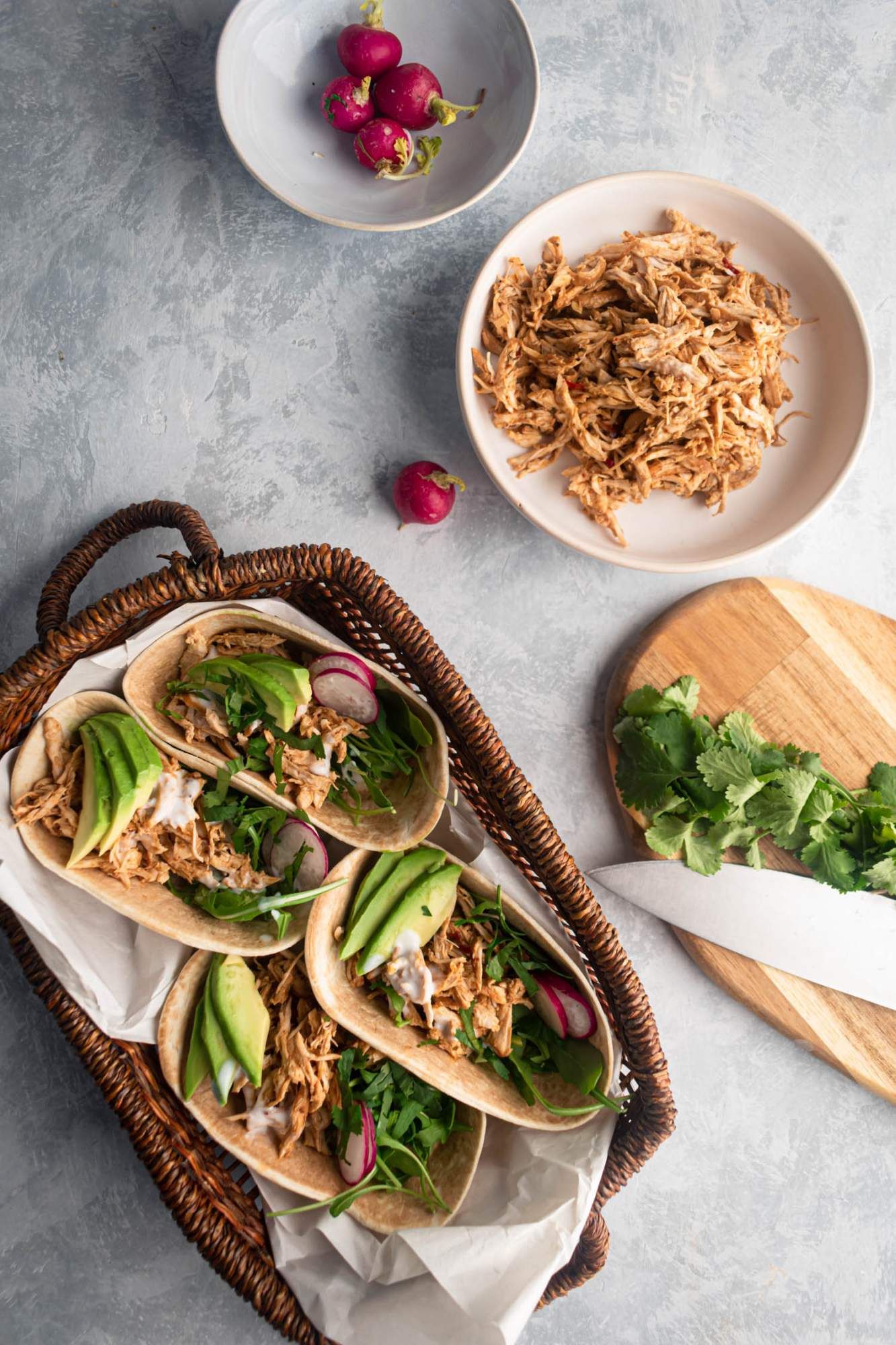 Chicken barbacao tacos with cilantro and avocado served in a basket with shredded chicken on the side.