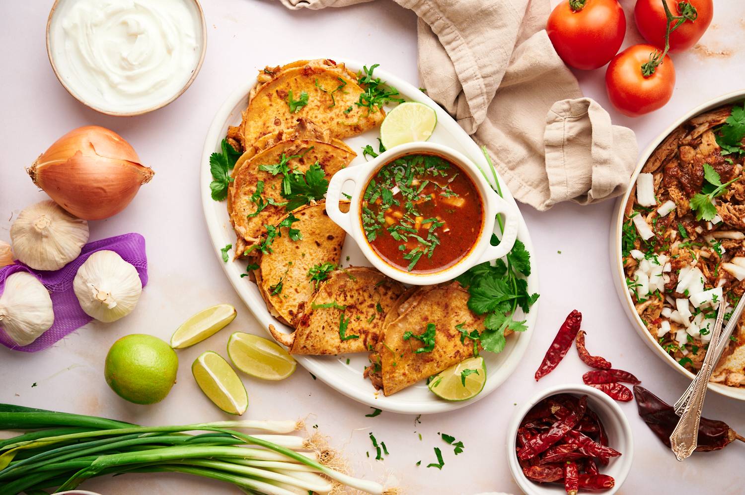 Tacos with chicken birria served on a plate with cialntro, consome, and limes. 