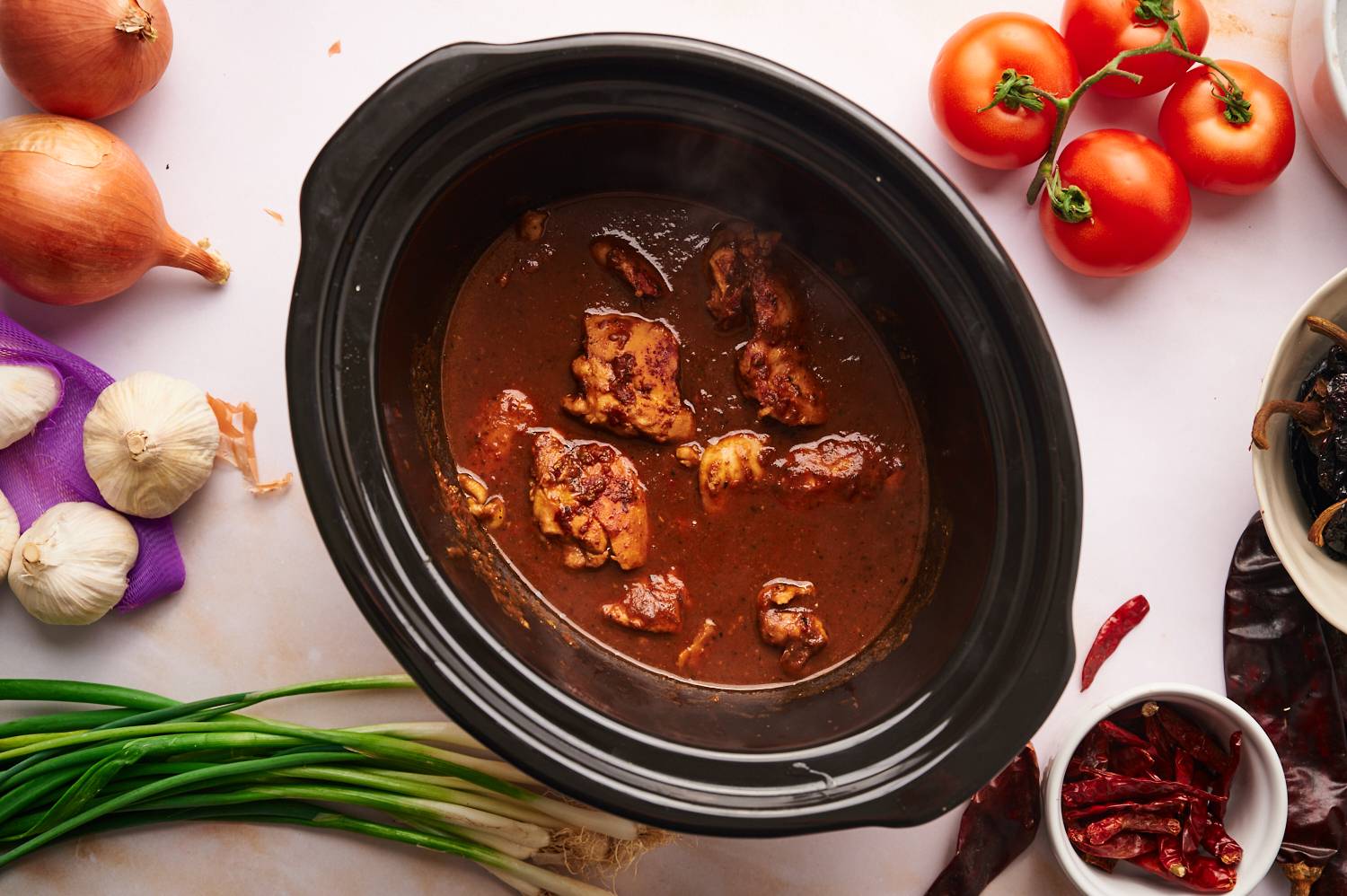 Birria de pollo in a slow cooker with a rich red chile sauce and cooked chicken thighs.