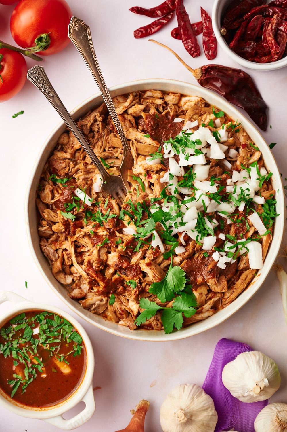 Birria chicken with red chile pepper sauce in a bowl with cilantro and onion.