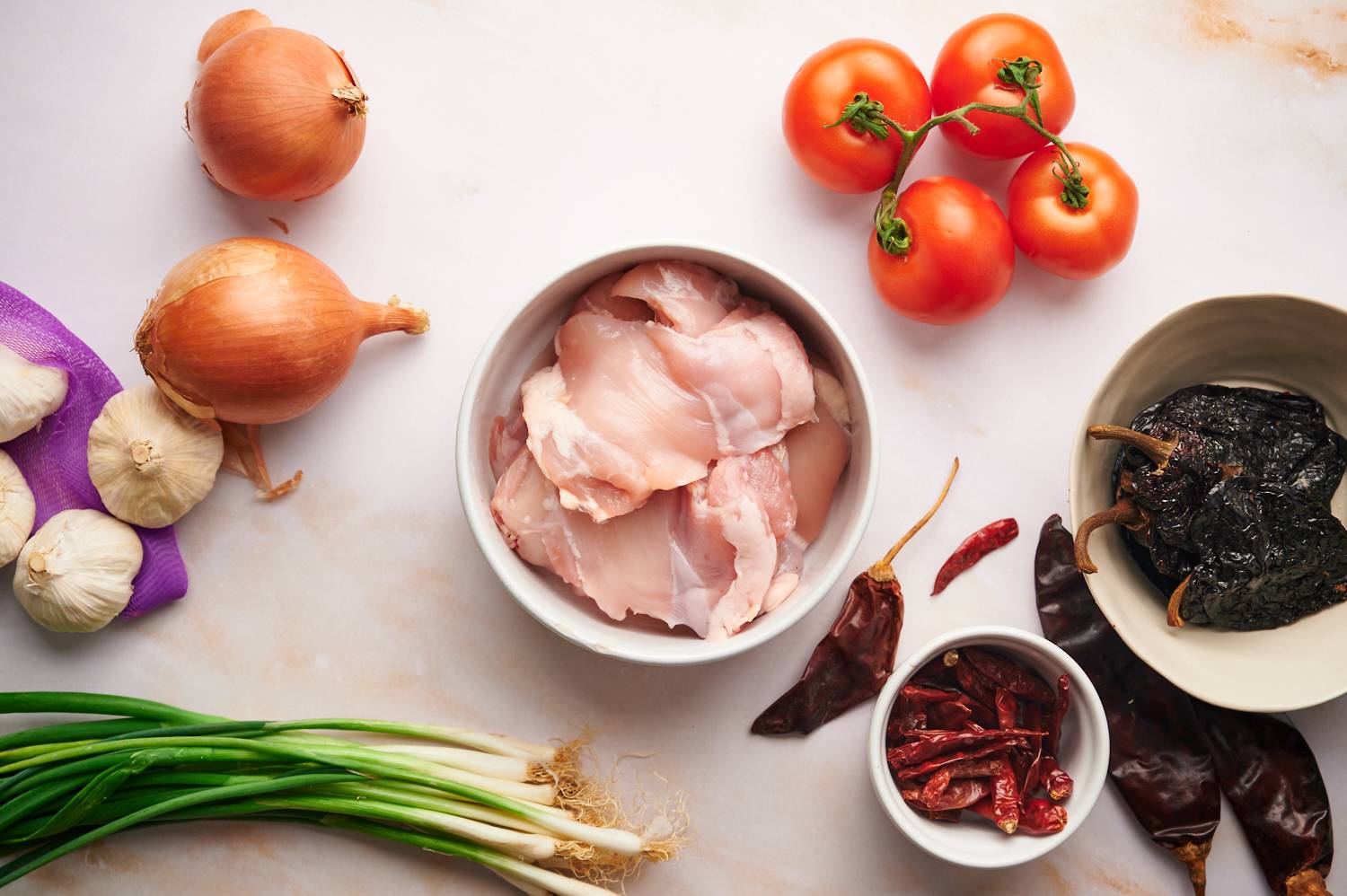 Ingredients to make chicken birria including tomatoes, onions, garlic, guajillo peppers, ancho peppers, and chile de arbol.