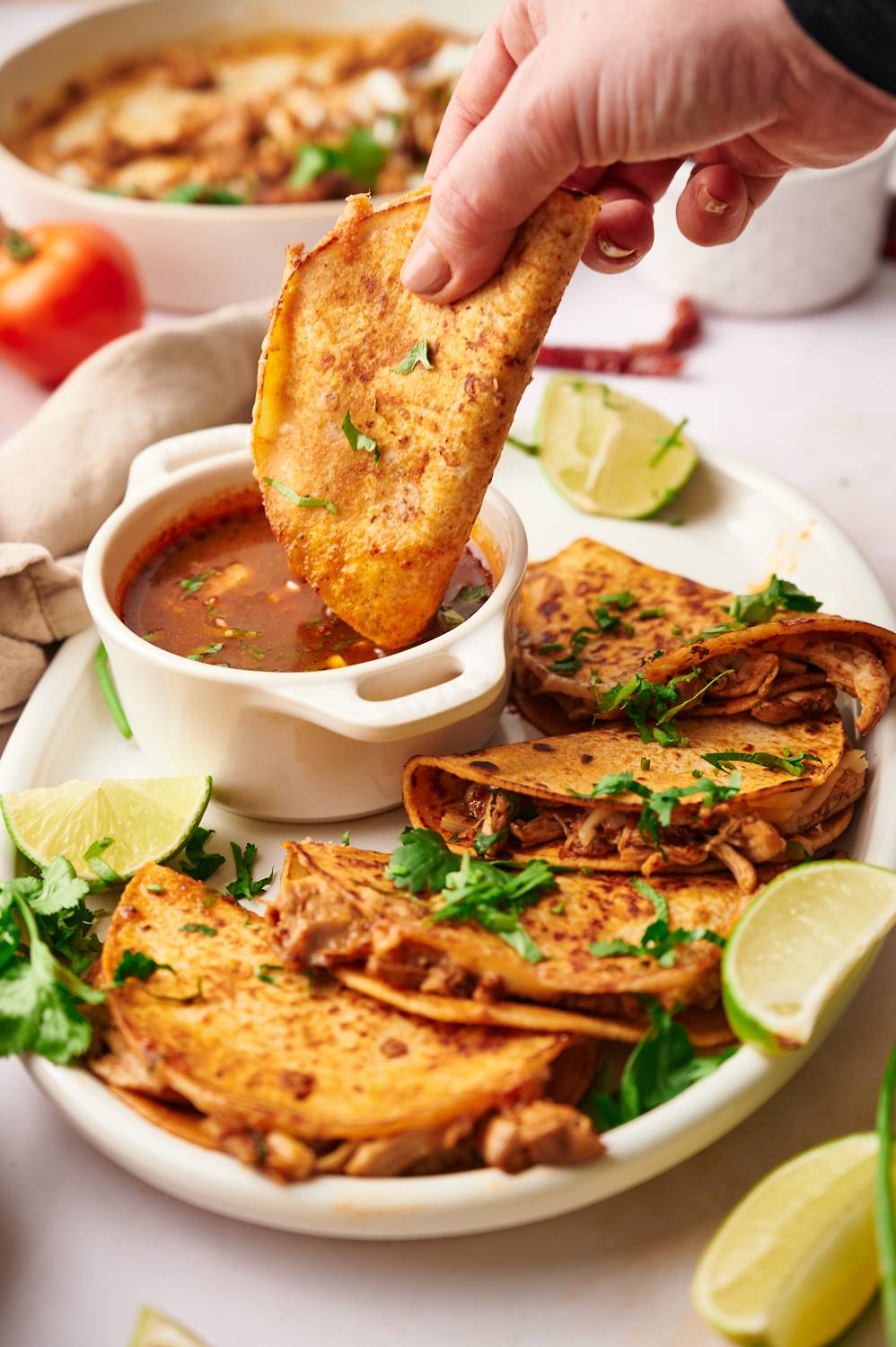 Birria chicken tacos cooked until crispy being dipped into a bowl of consommé with cilantro and onion.