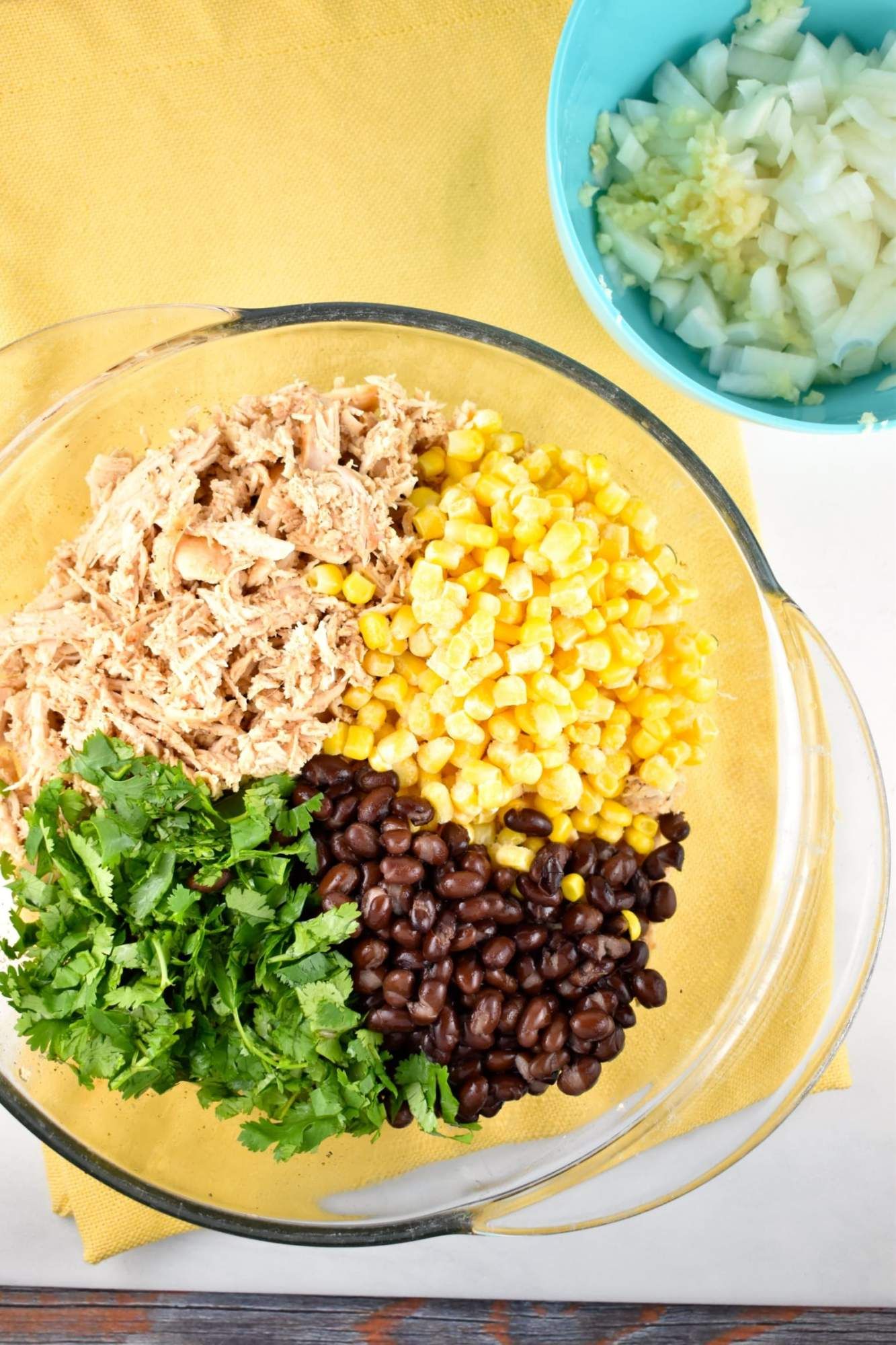 Chicken, black beans, cilantro, and corn in a glass bowl with a yellow napkin.