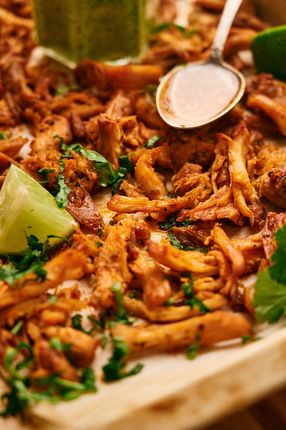 Crispy carnitas with chicken on a baking sheet with browned crispy edges, limes, and cilantro.