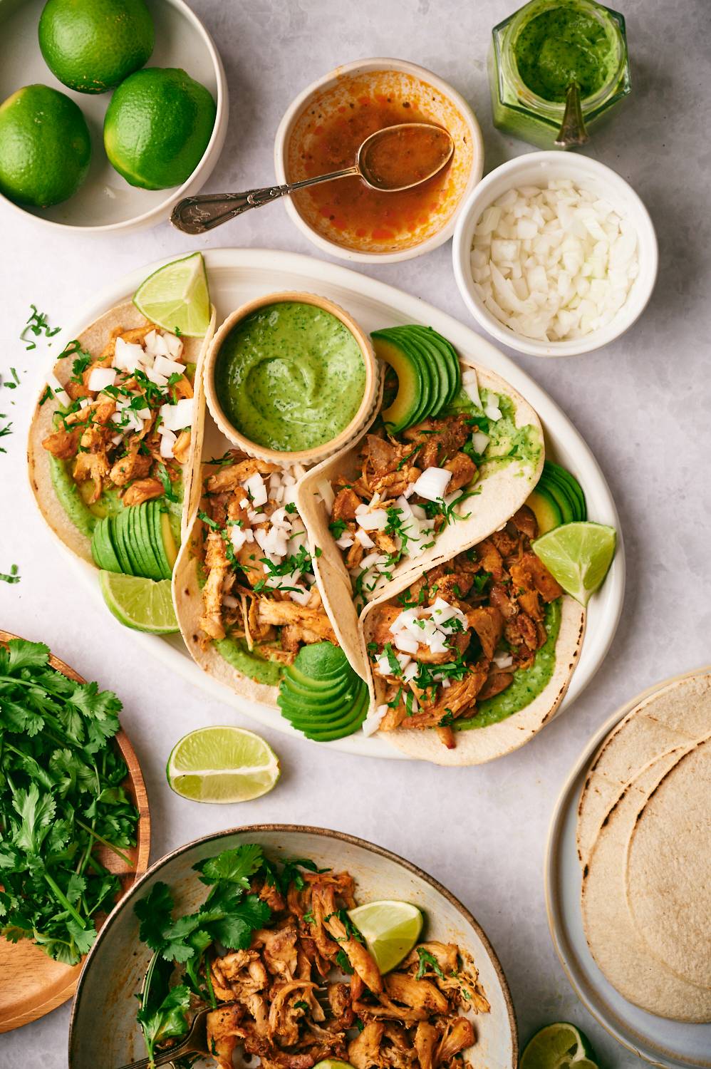 Tacos with chicken carnitas, avocado salsa, limes, cilantro, and white onions.