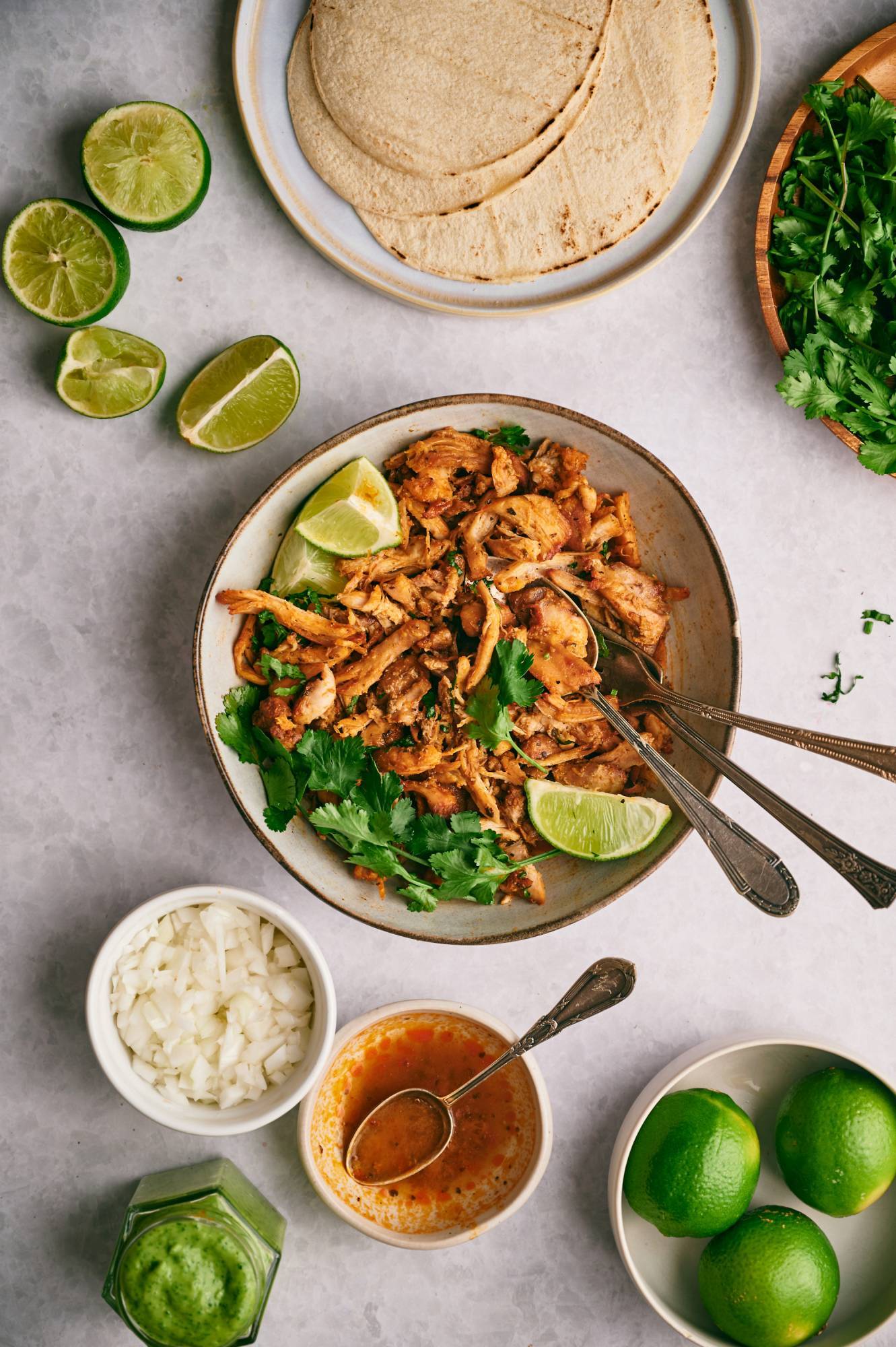 Chicken carnitas in a bowl with cilantro and limes with corn tortillas on the side.