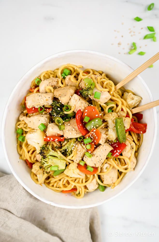 Chow mien with chicken, veggies, noodles, and green onions in a white bowl.