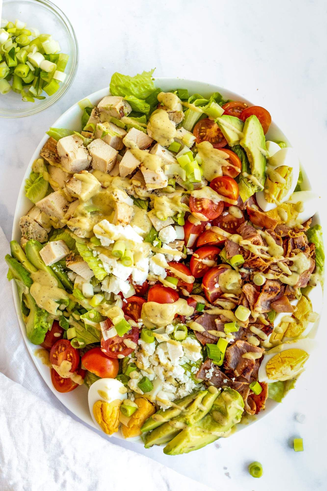 Cobb salad with chicken, eggs, blue cheese, tomatoes, bacon, and a mustard dressing in a bowl.