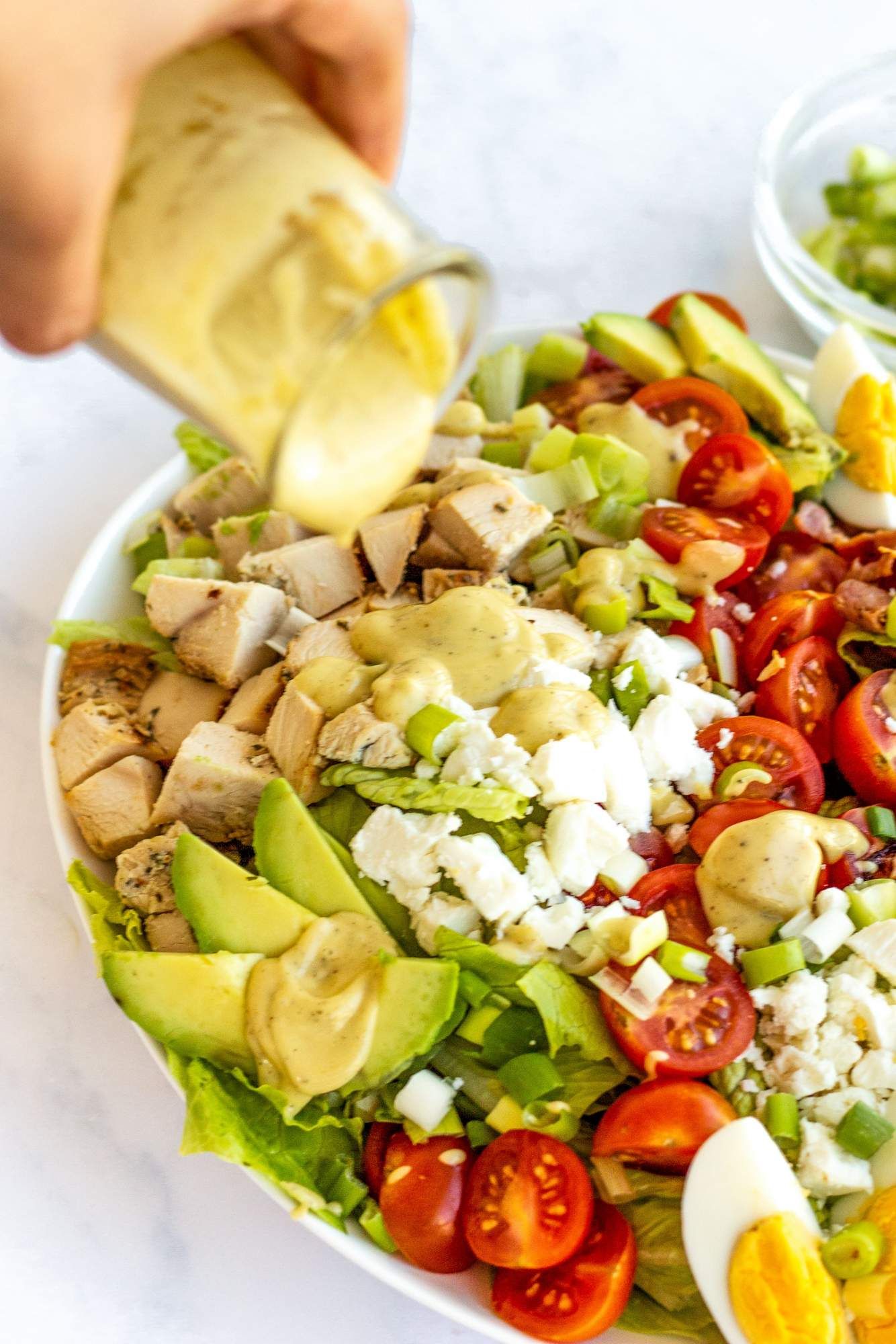 Dressing being poured over a Chicken Cobb Salad with blue cheese, eggs, and bacon.