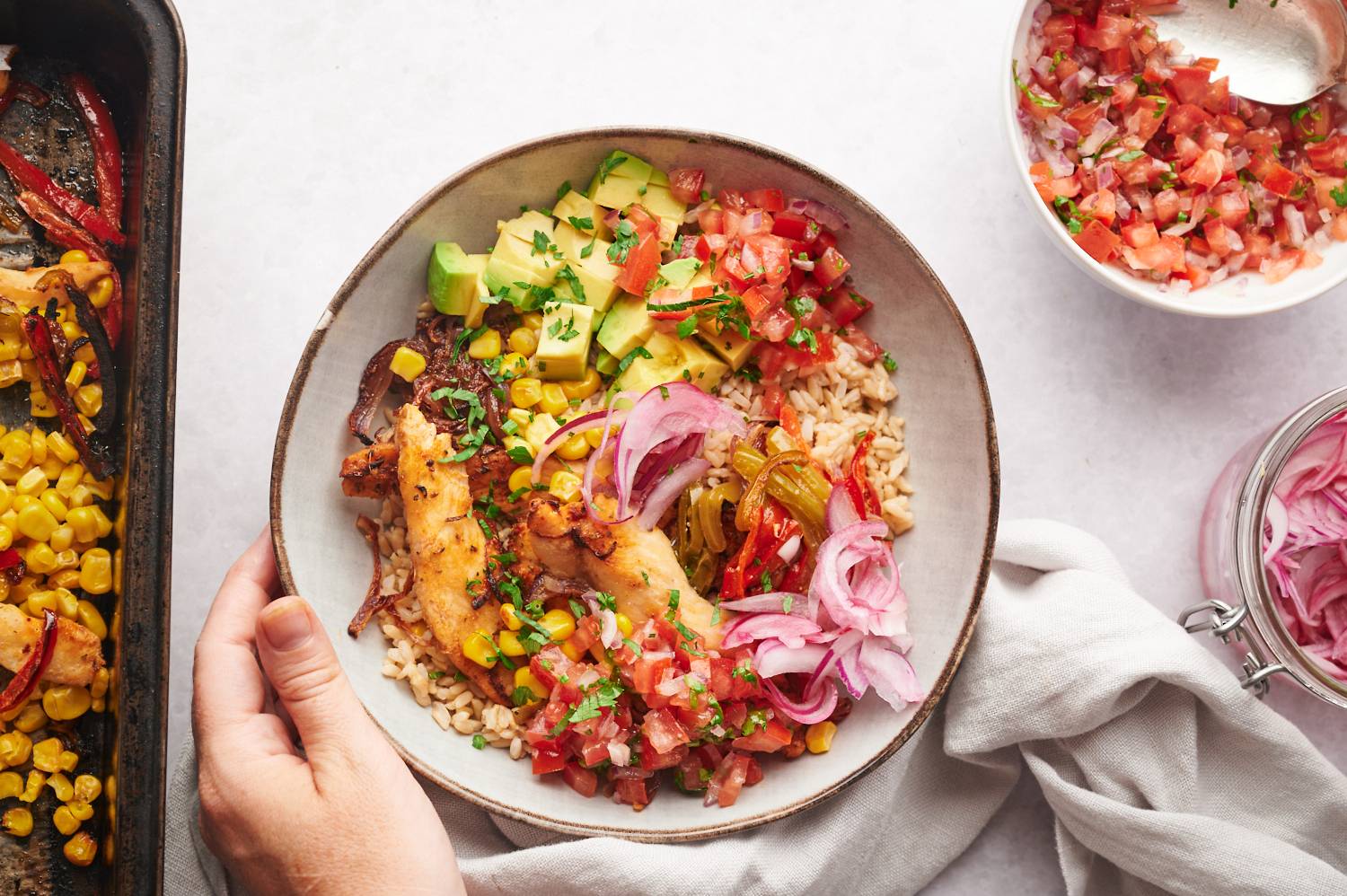 Chicken fajiat rice bowls with avocado, corn, bell peppers, onions, pico de gallo, brown rice, and cilantro.