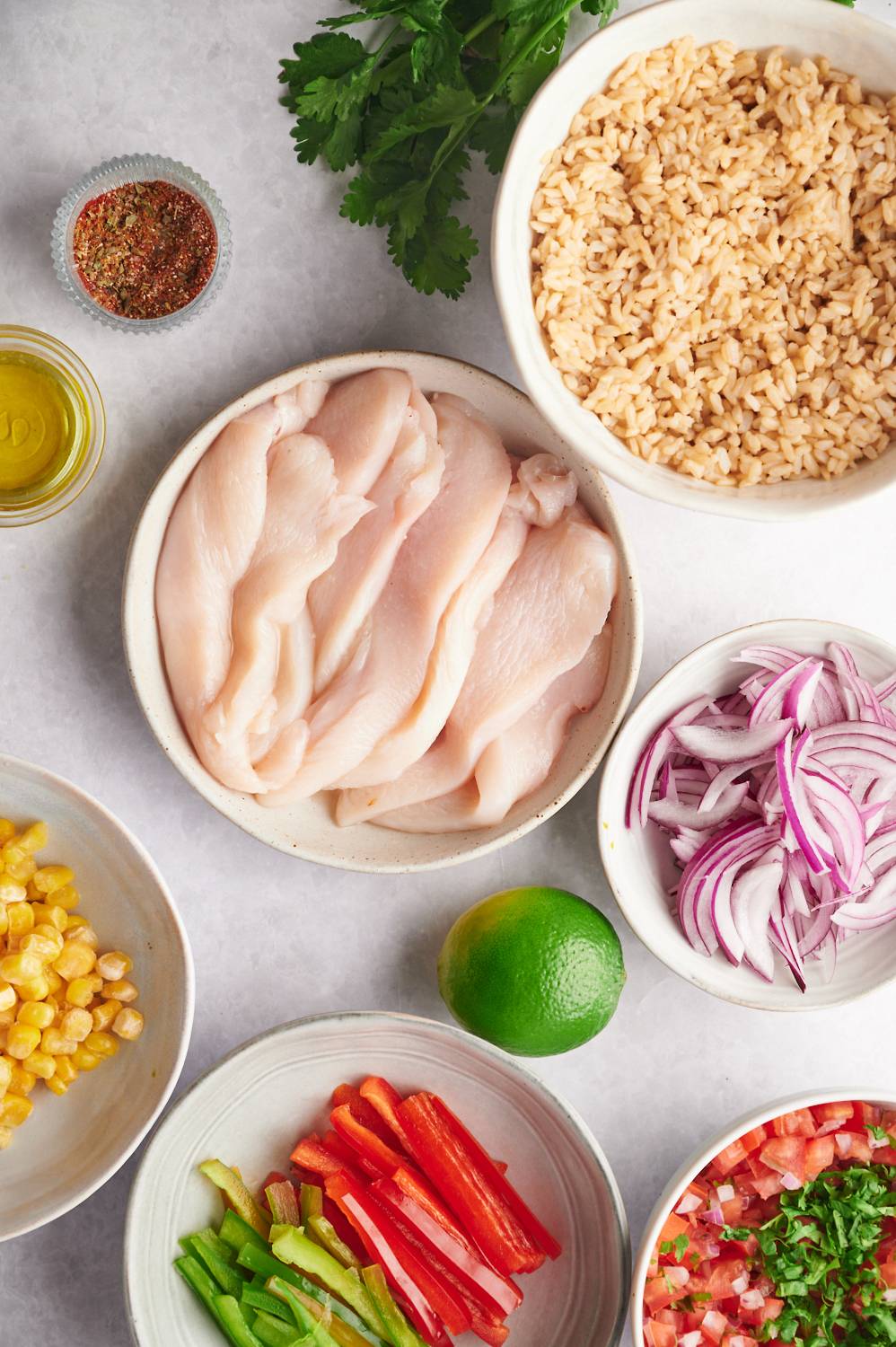 Ingredients for fajita bowls including chicken, bell peppers, red onion, pico de gallo, rice, limes, and fajita seasoning.