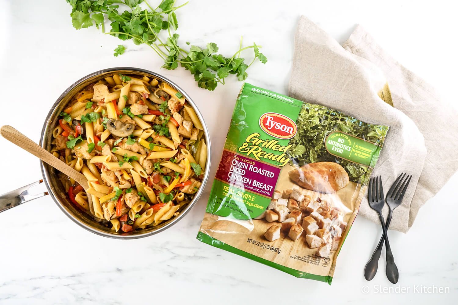 Pan of fajita chicken pasta with a bag of Tyson chicken strips, cilantro, and two forks.