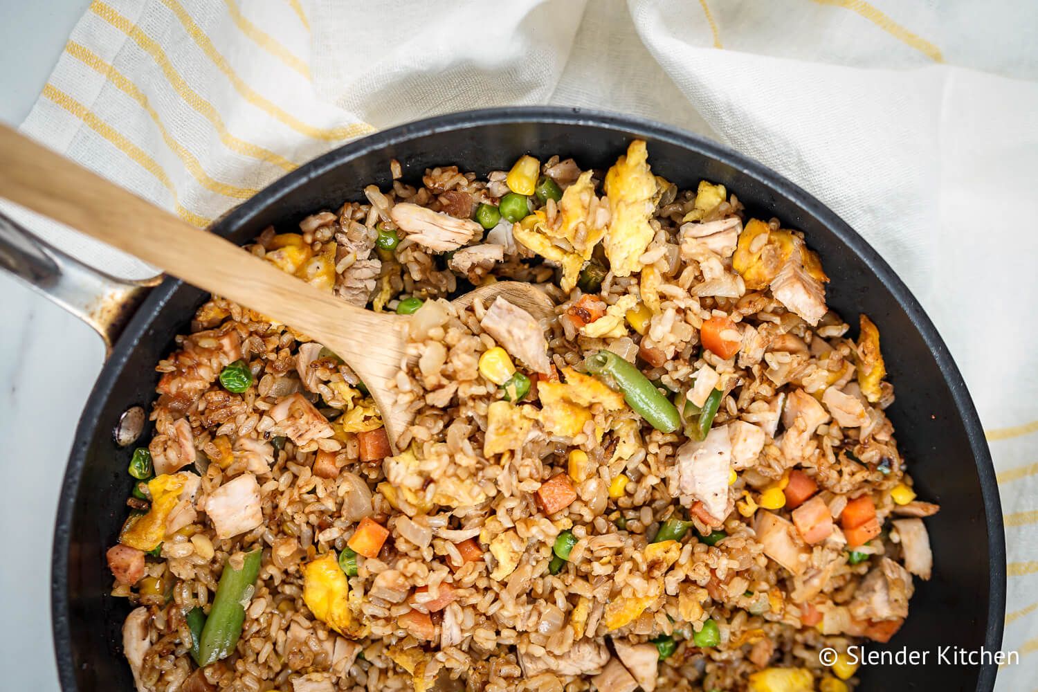 Fried rice with chicken in a skillet with peas, carrots, eggs, and green beans.