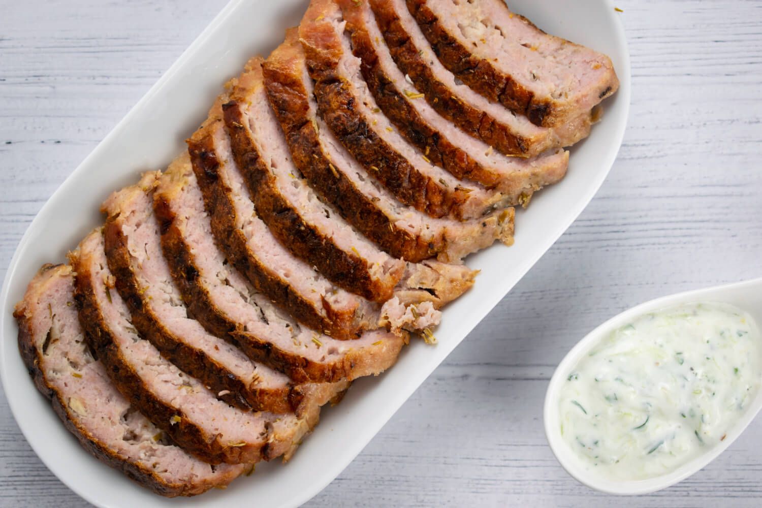 Homemade chicken gyros sliced in a white dish with tzatziki on the side.