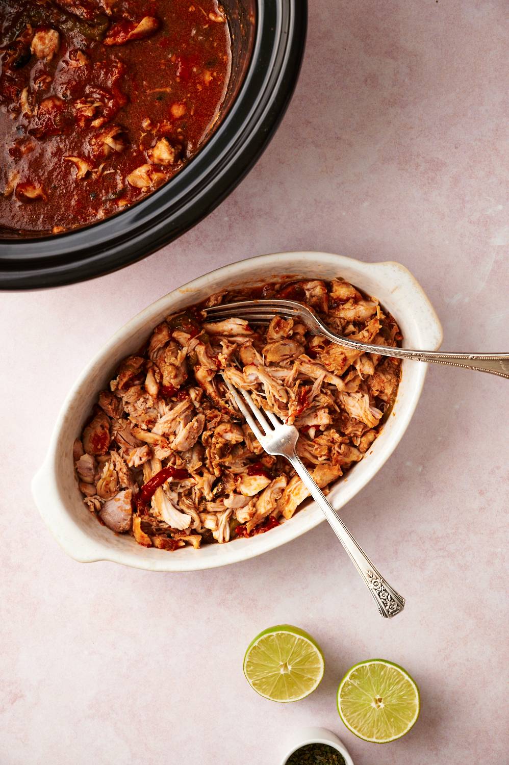 Machaca de pollo shredded in a dish with two forks with limes on the side.