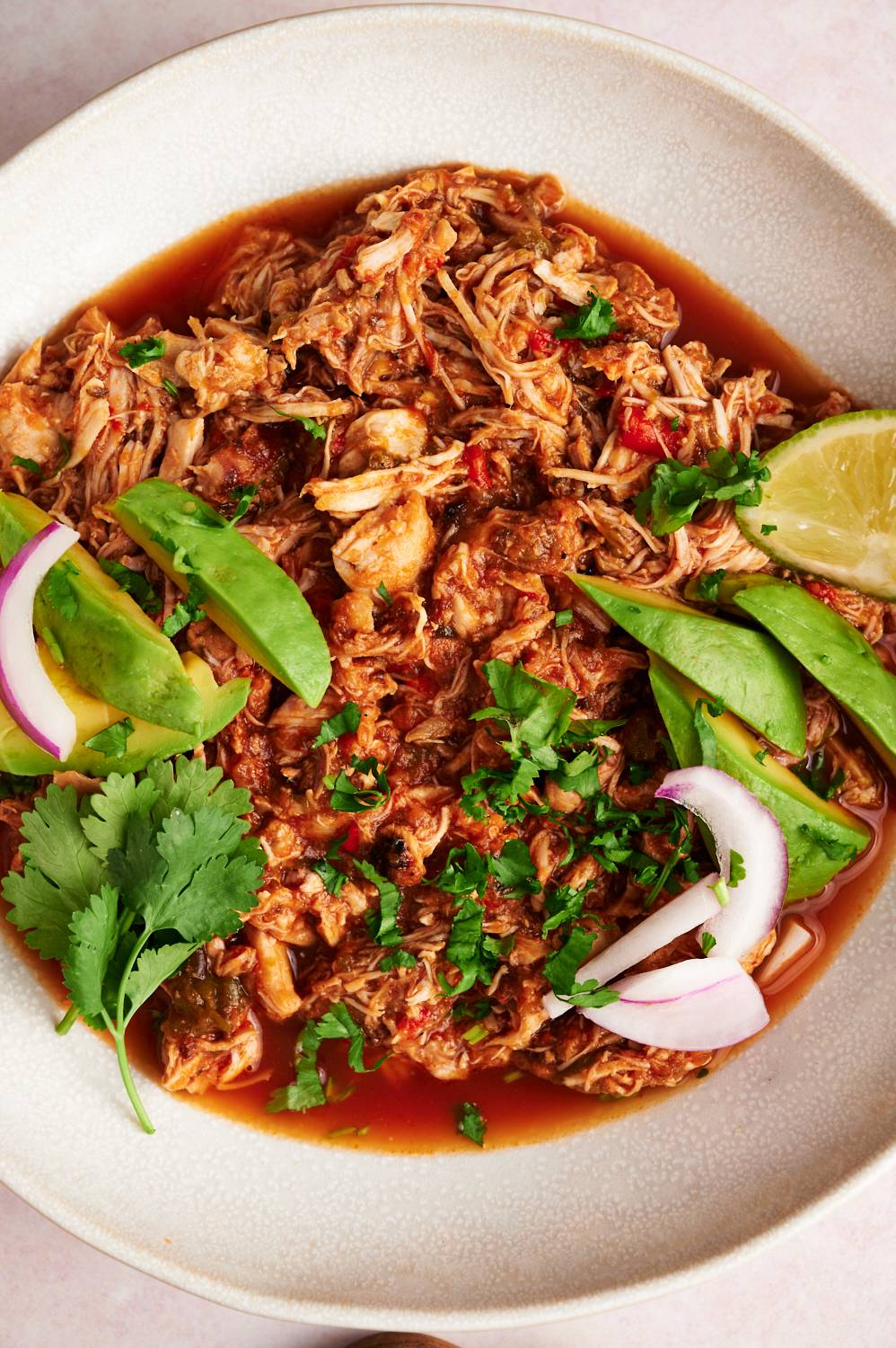 Mexican chicken machaca with shredded chicken in a spicy red sauce served with avocado, cilantro, and onion.