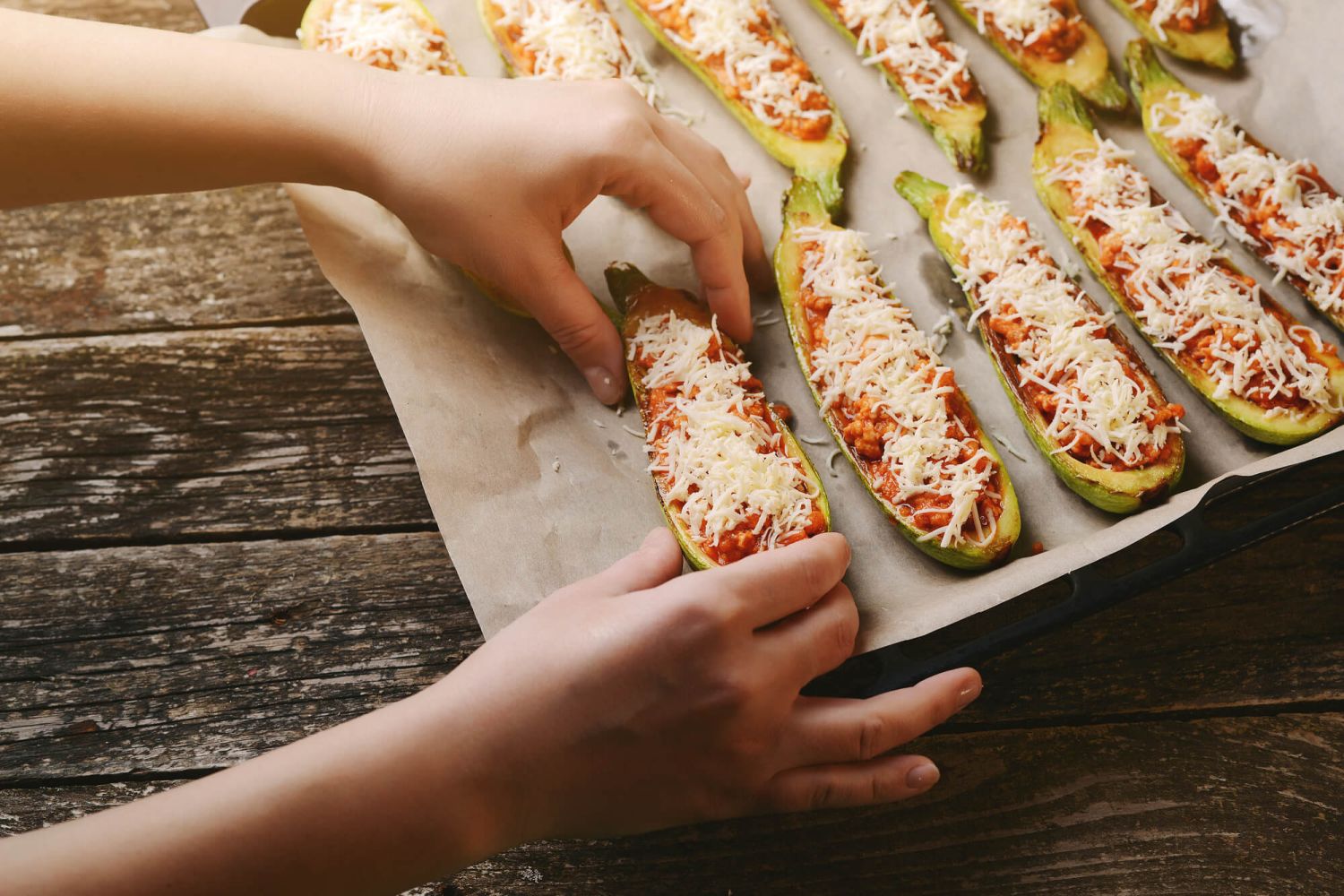 Chicken parmesan zucchini boats with a hand sprinkling cheese on top.