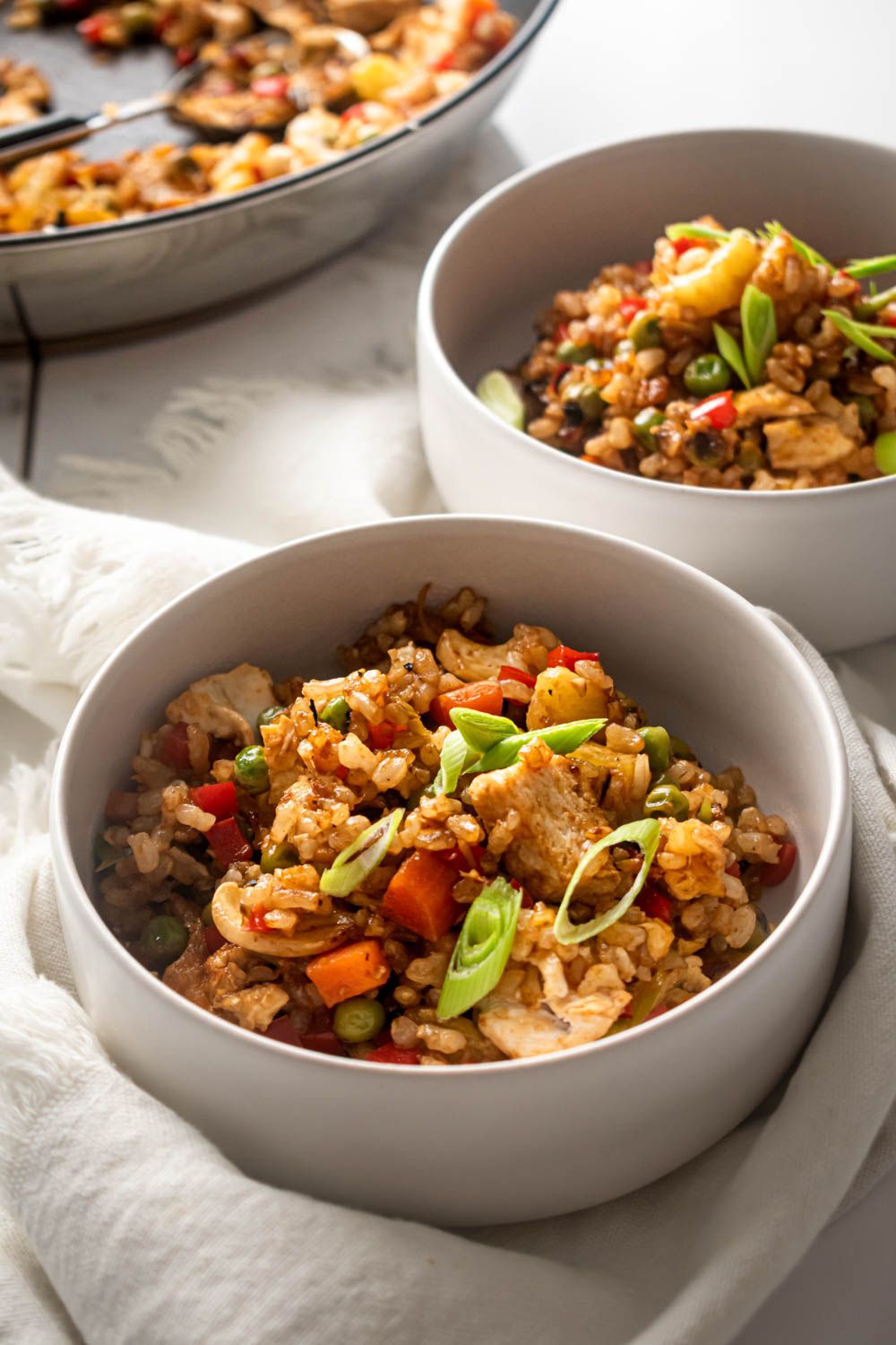 Pineapple fried rice with chicken breast, red peppers, peas, carrots, and brown rice served in two bowls.