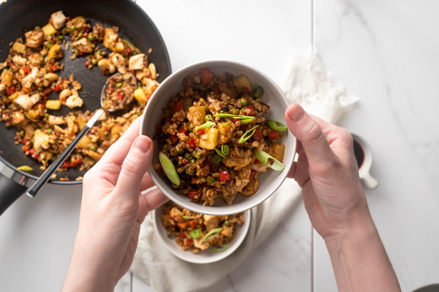 Chicken fried rice with pineapples, cashews, green onions, and vegetables in a bowl being held up by two hands.