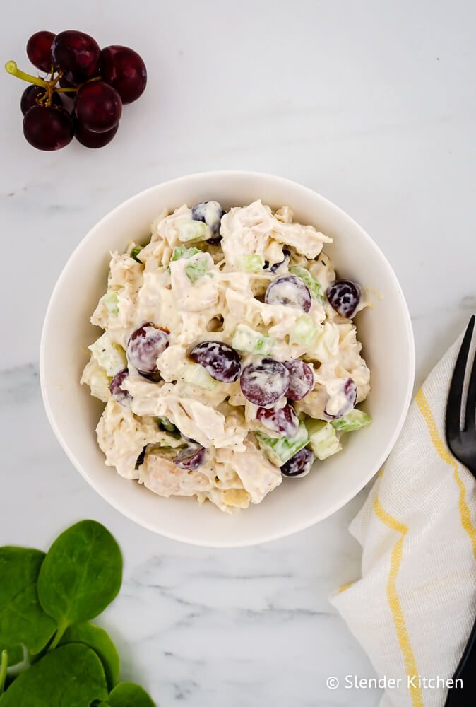 Grape chicken salad with chicken breast, celery, yogurt, and mustard in a bowl with spinach on the side.