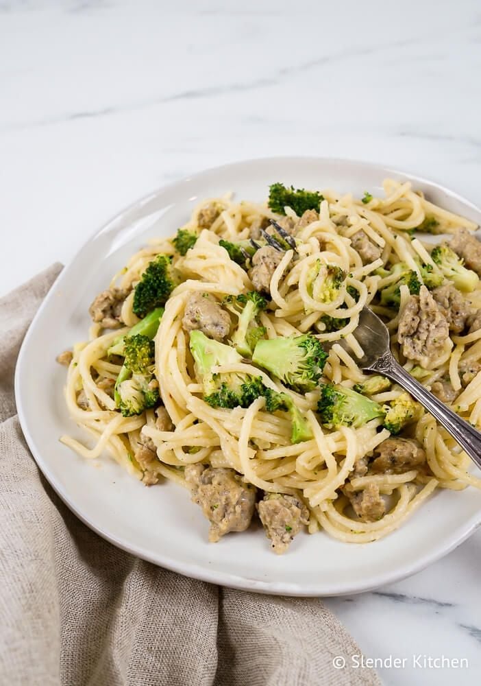 Chicken sausage pasta with spaghetti, broccoli, and Parmesan cheese on a plate with a fork.