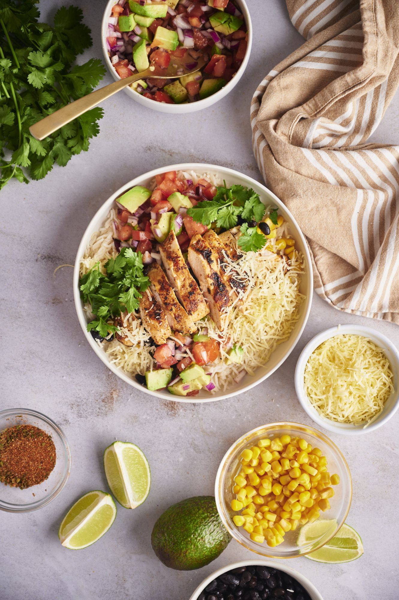 Taco bowls with chicken, rice, black beans, corn, pico de gallo, and shredded cheese in a white bowl.