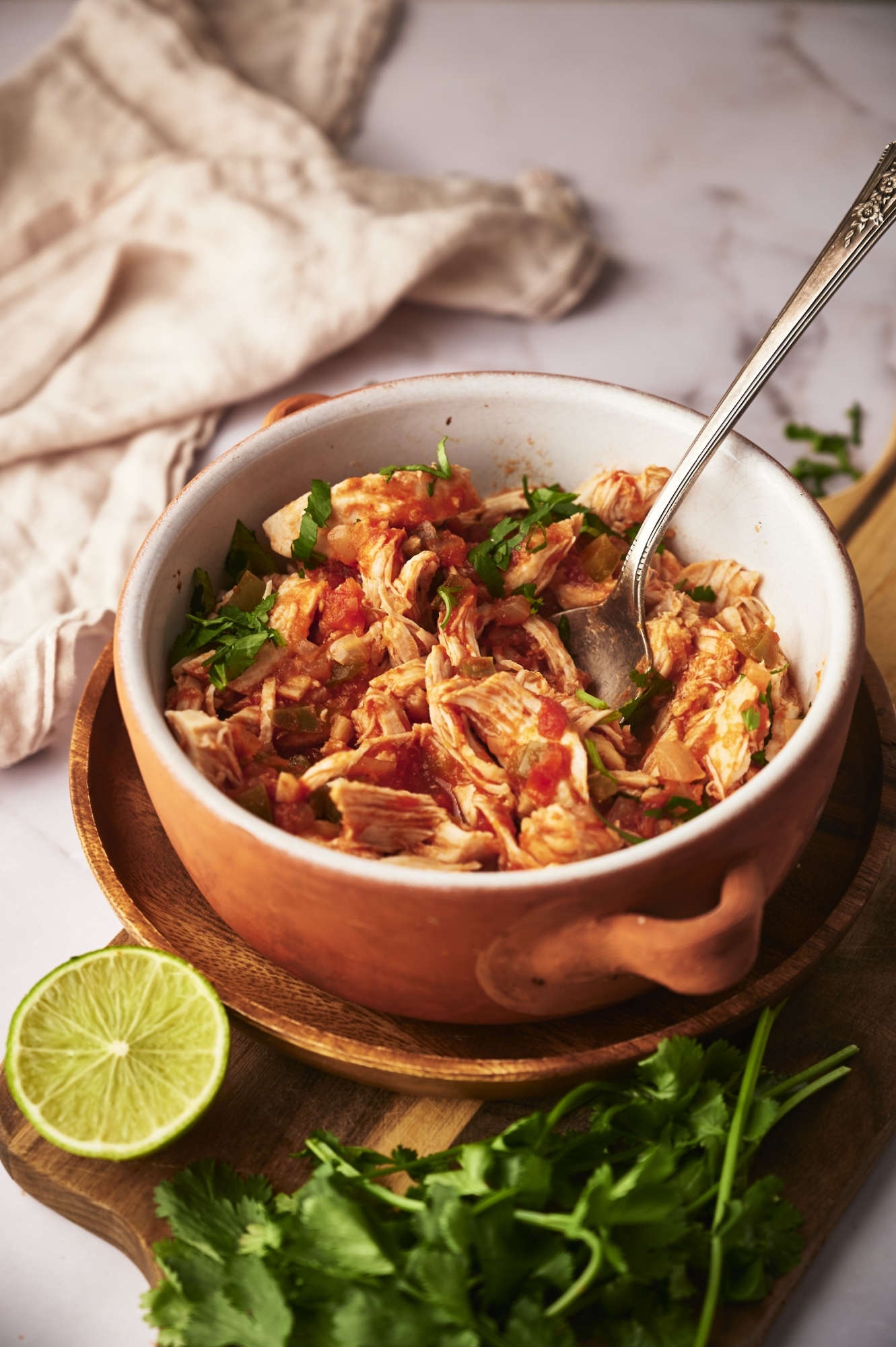 Mexican chicken tinga in a bowl with tomato chipotle sauce with cilantro and lime on the side.