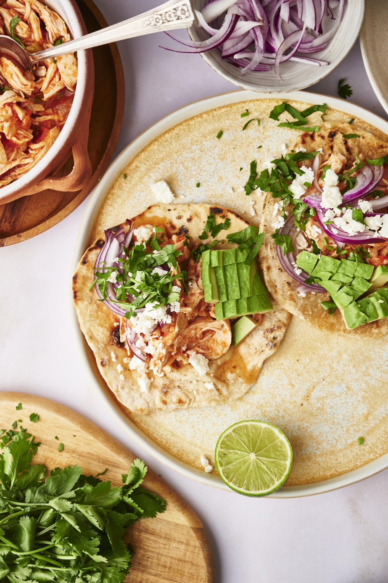 Chicken tinga tacos with queso fresco, cilantro, red onion, and avocado on a corn tortillas.