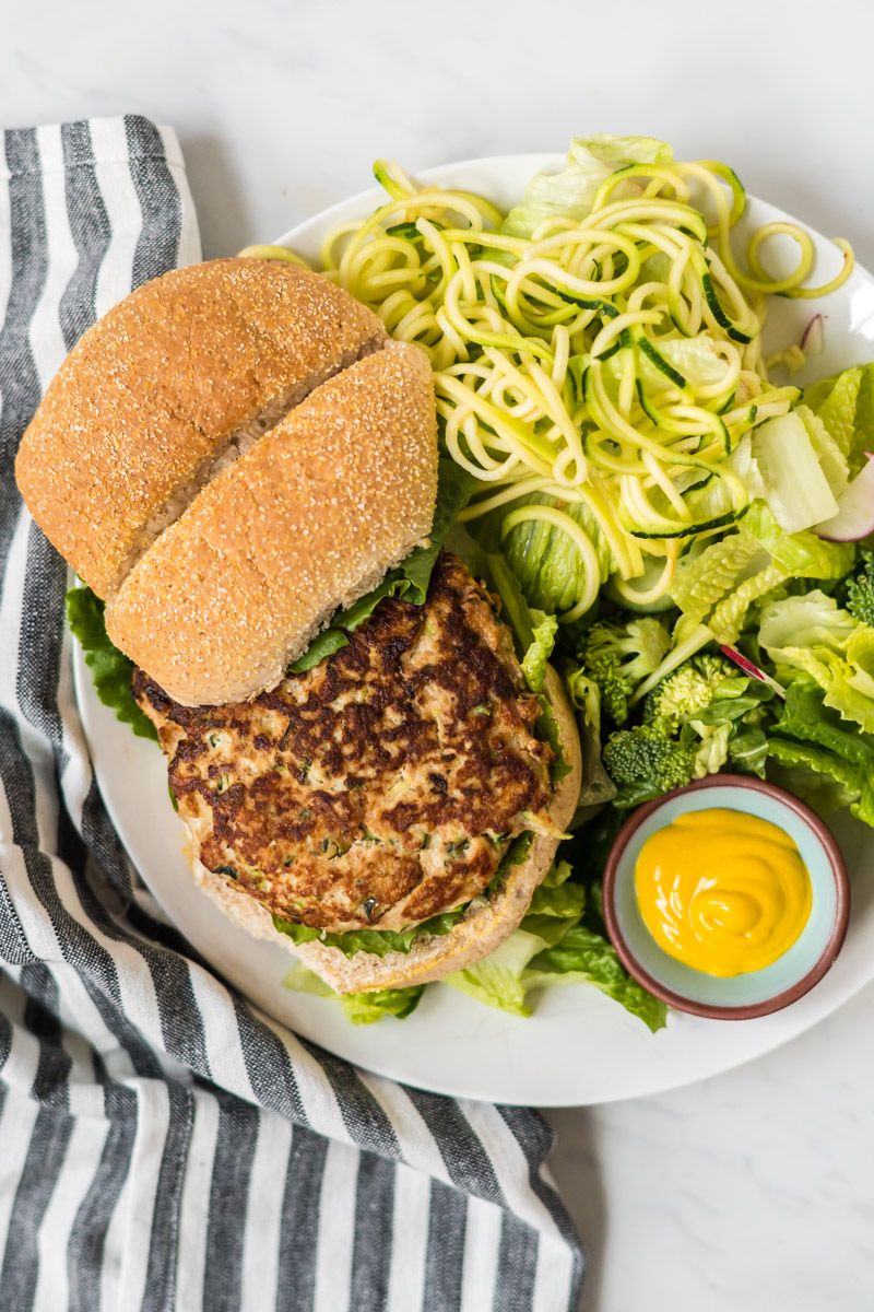 Chicken burgers with zucchini and herbs on a plate with a whole wheat bun and mustard.