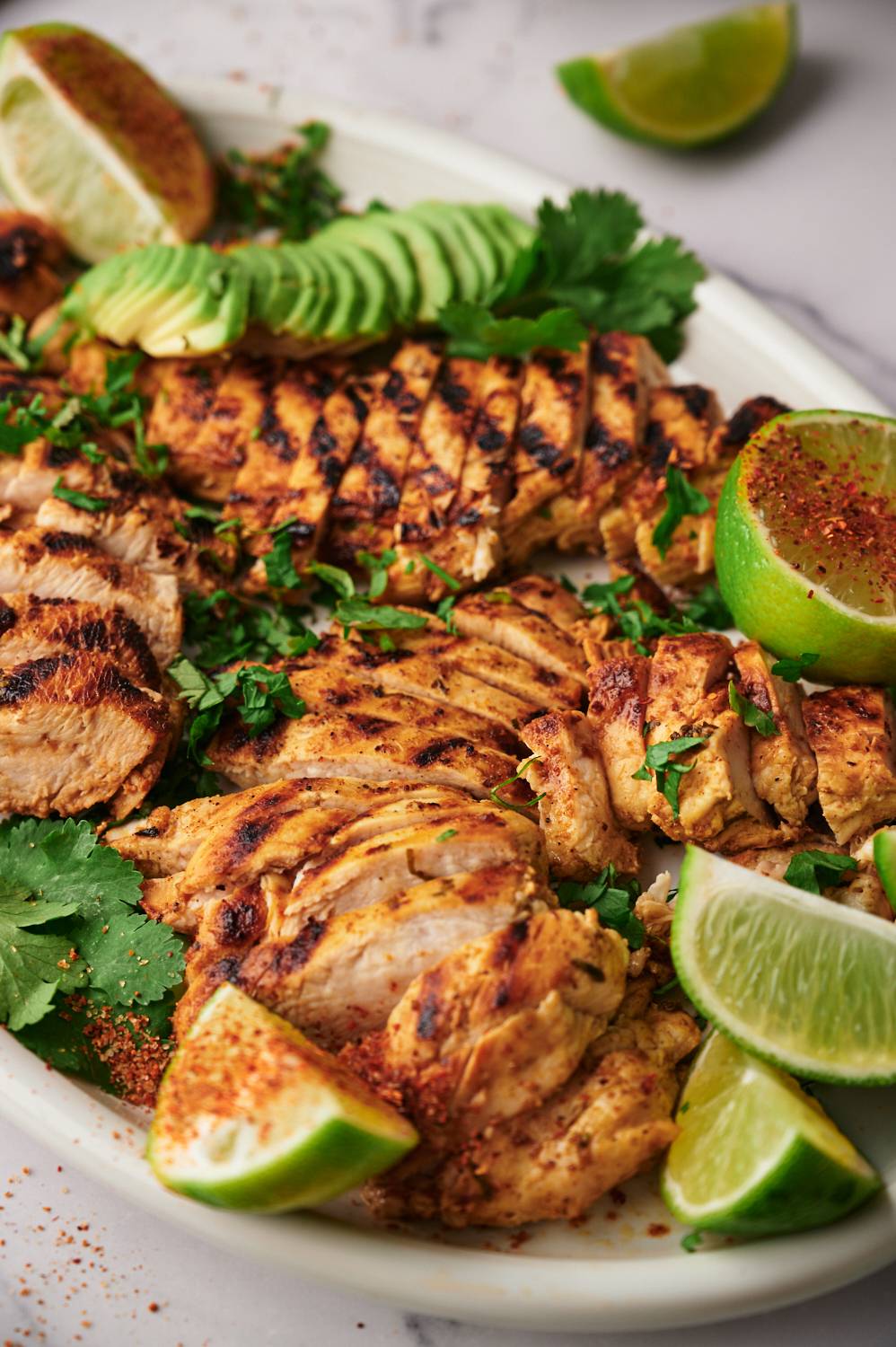 Grilled chili lime chicken served on a platter with avocado, limes, cilantro, and chili powder.