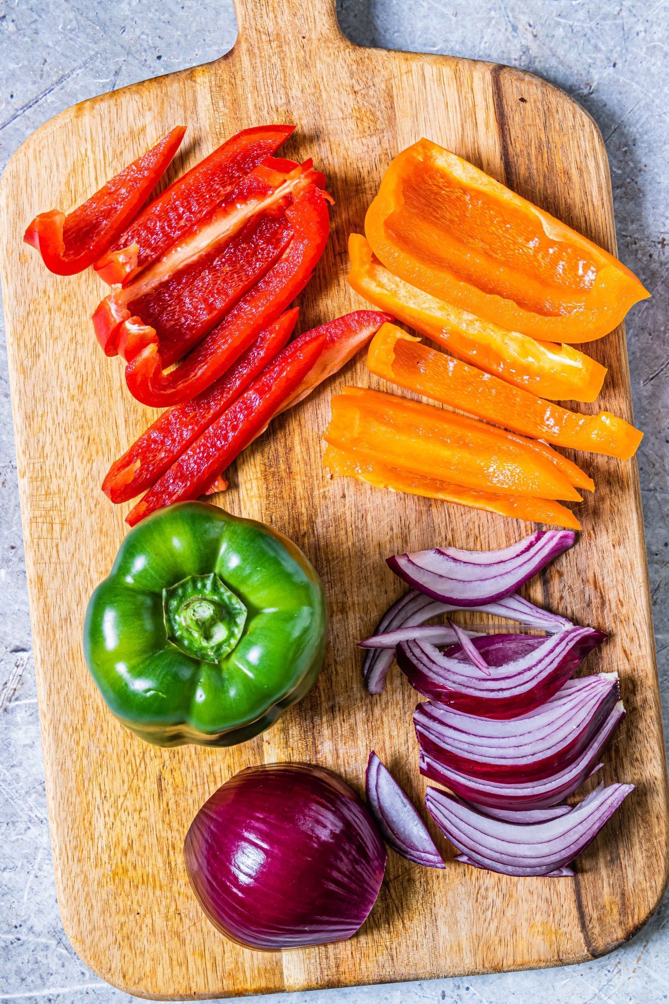 Sliced bell pepper and red onions on a wooden cutting board.