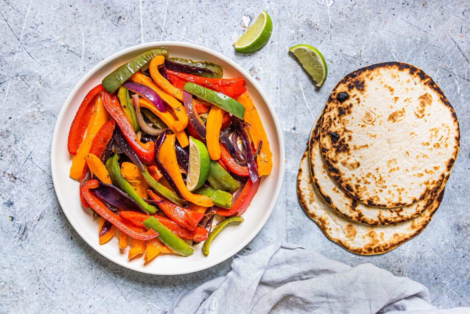 Fajita veggies inspired by Chipotle restaurant on a plate with charred tortillas on the side.