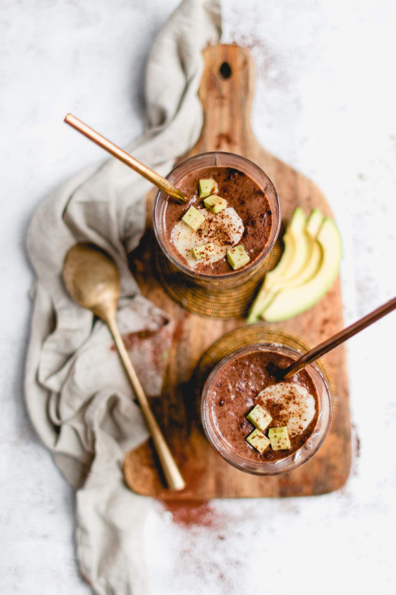 Avocado smoothie with chocolate in two glasses with small pieces of avocado on top.