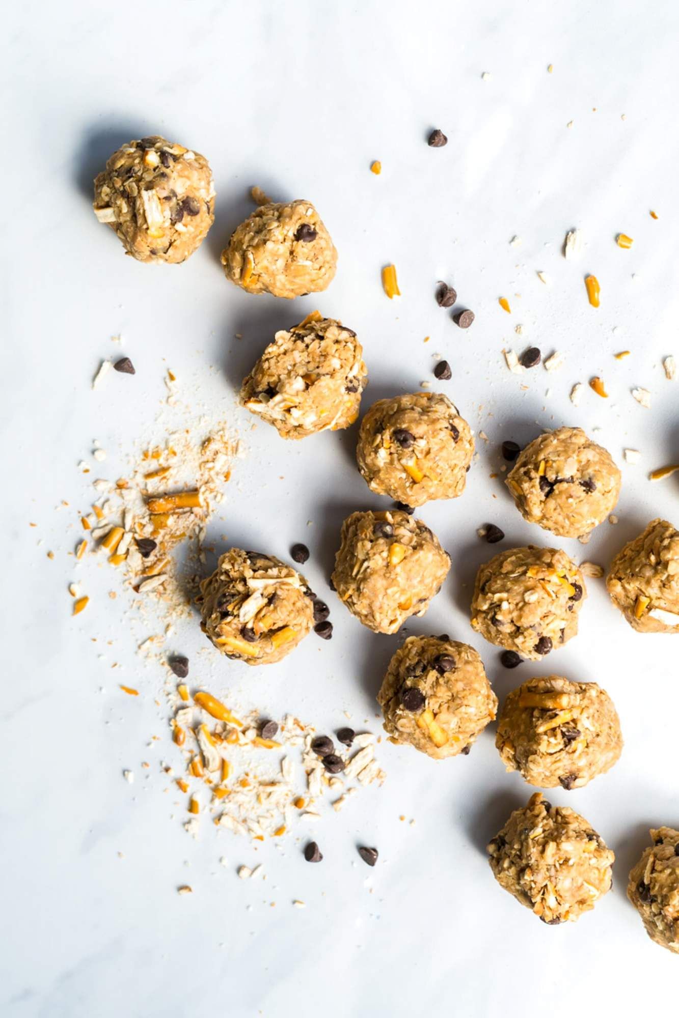 Peanut butter energy balls with chocolate chips and oats on a marble board with pretzels.