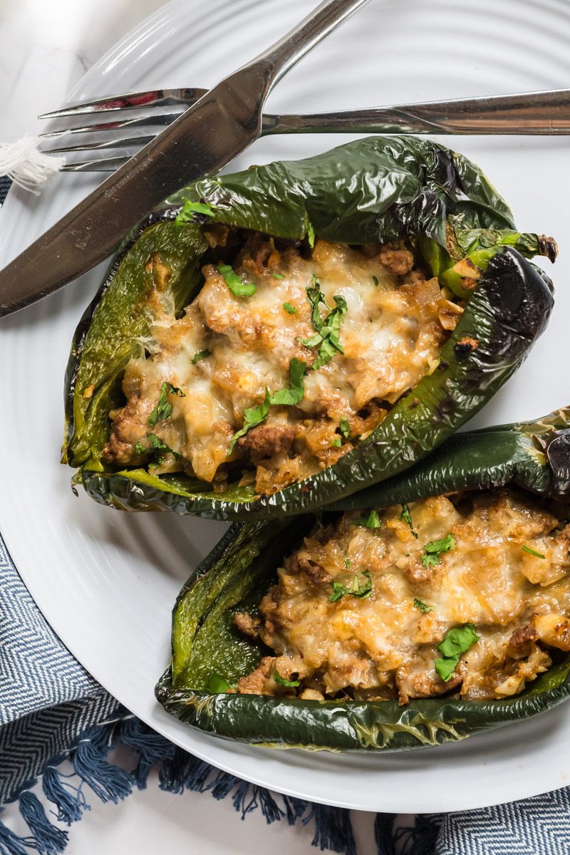 Stuffed poblanos with ground turkey and melted cheese  on a plate with a knife and fork.