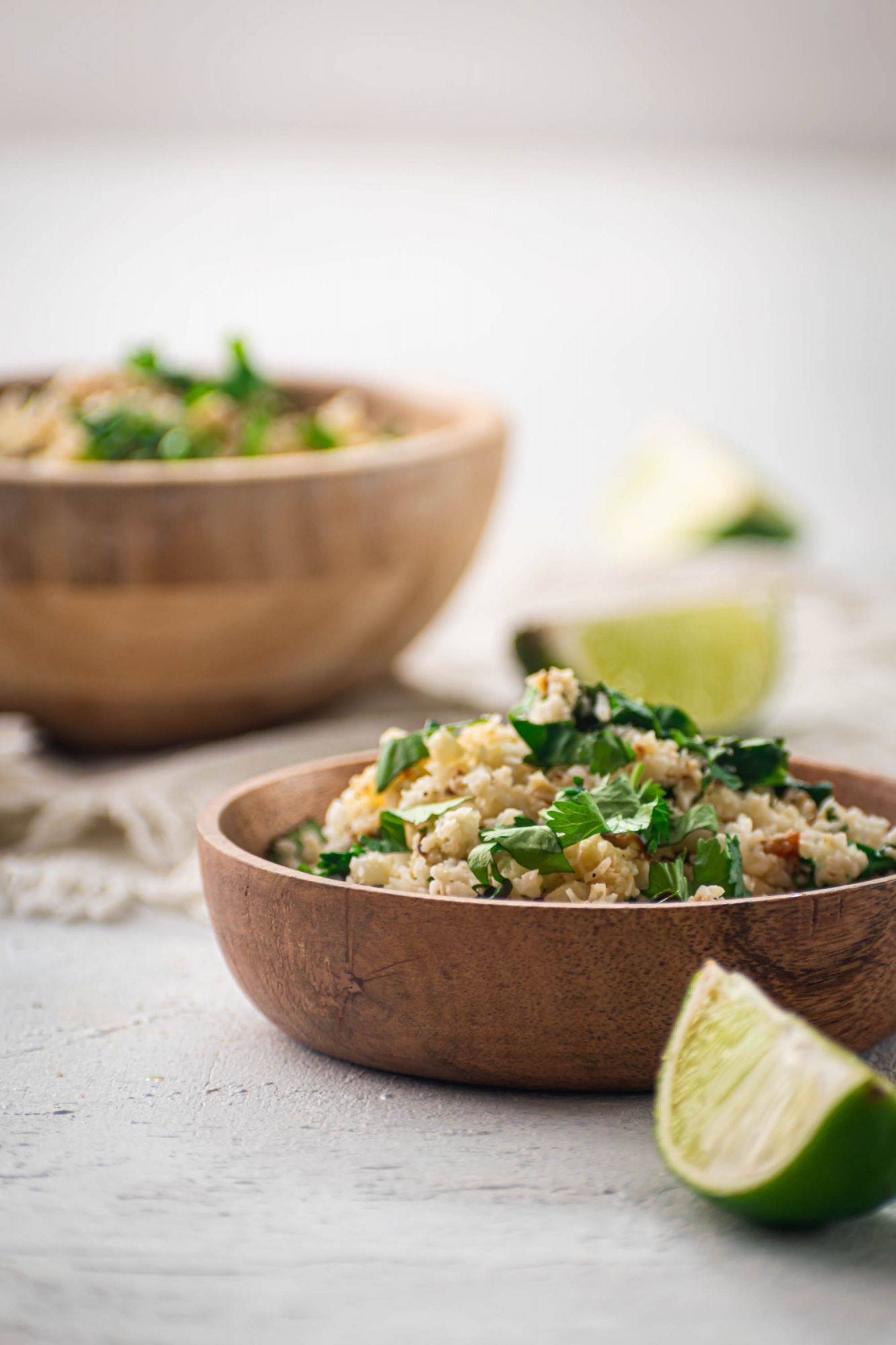 Low carb cauliflower rice cooked with fresh cauliflower, lime juice, and cilantro served in two wooden bowls.