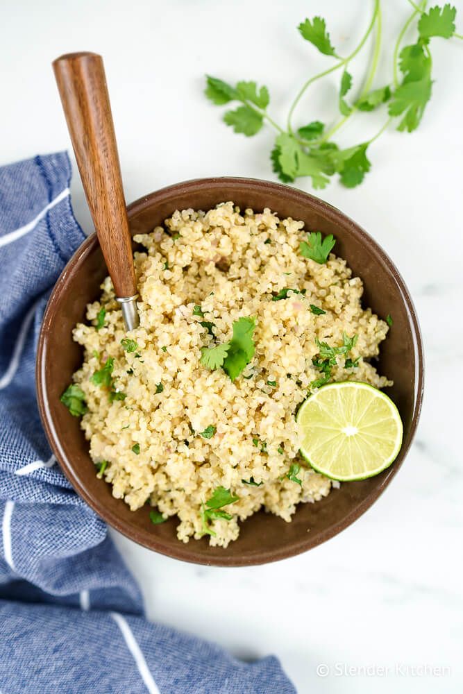 Quinoa with lime and cilantro in a bowl with a wooden spoon and fresh lime juice and cilantro.