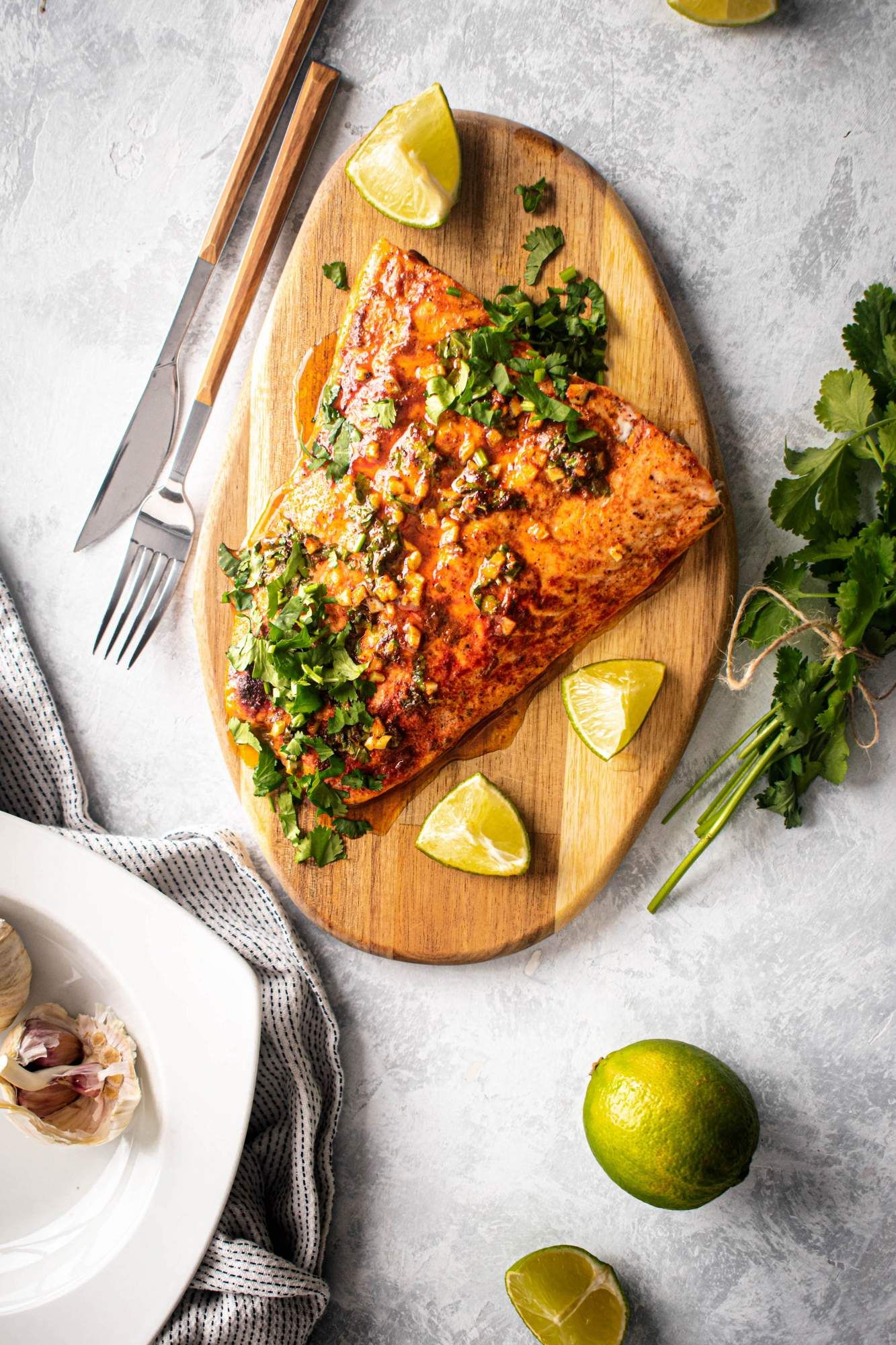 Salmon with cilantro lime sauce on a wooden board with lime wedges and garlic on the side.