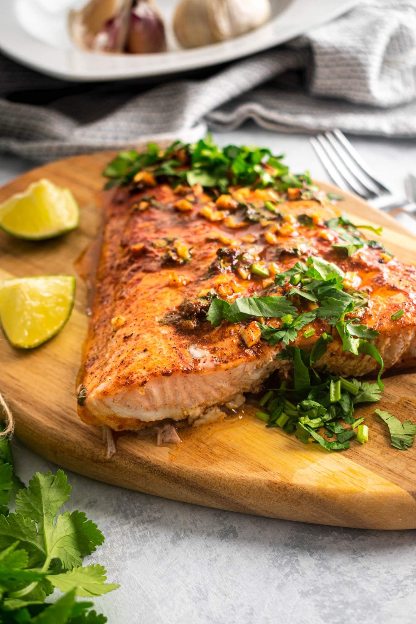 Baked cilantro lime salmon on a wooden board with fresh cilantro, garlic, lime juice, and honey on top.